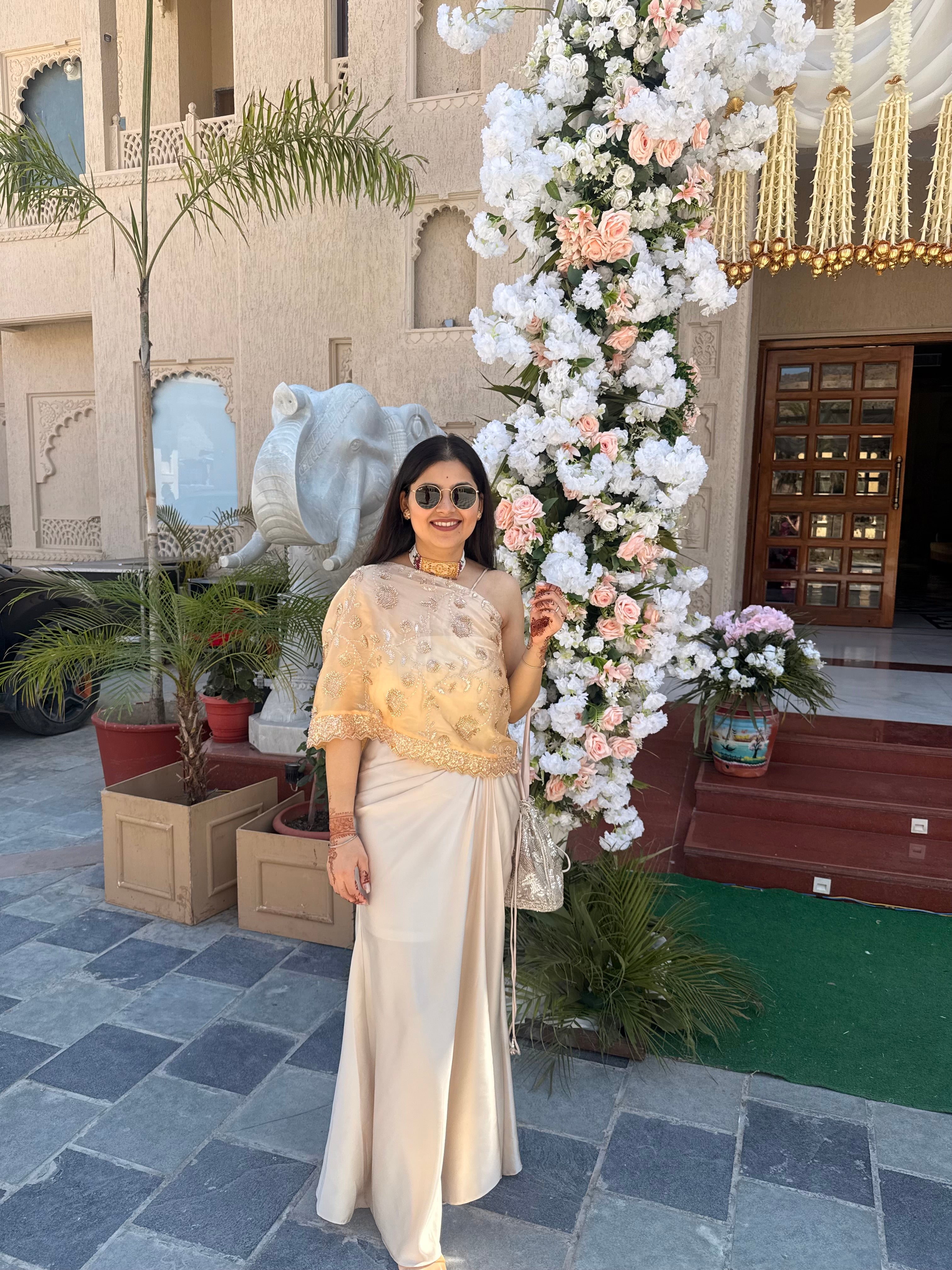 A flowy champagne drape skirt paired with embroidered one shoulder sheer cape blouse, designed to bring together timeless tradition and contemporary style.