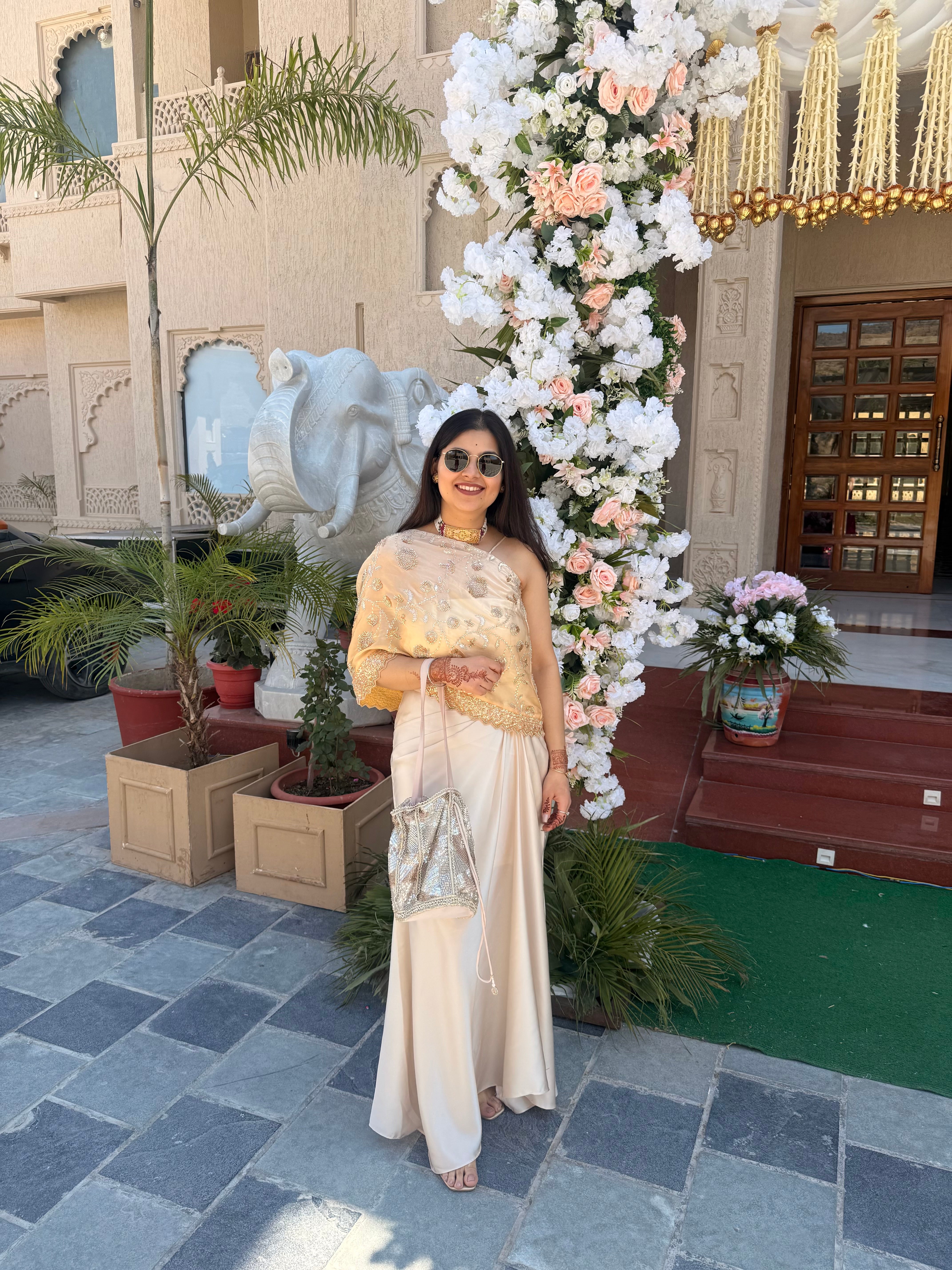 A flowy champagne drape skirt paired with embroidered one shoulder sheer cape blouse, designed to bring together timeless tradition and contemporary style.
